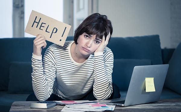 Portrait of worried and desperate woman feeling stressed paying credit card debts and bills on laptop computer on sofa at home. In business and home finances and financial problems concept.